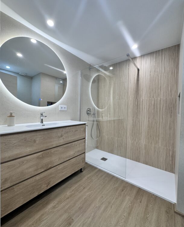 Reforma de baño en Esplugues realizada por Grup Innova. Ducha antideslizante, grifería empotrada, suelo vinílico SPC y diseño moderno en tonos madera y beige piedra.