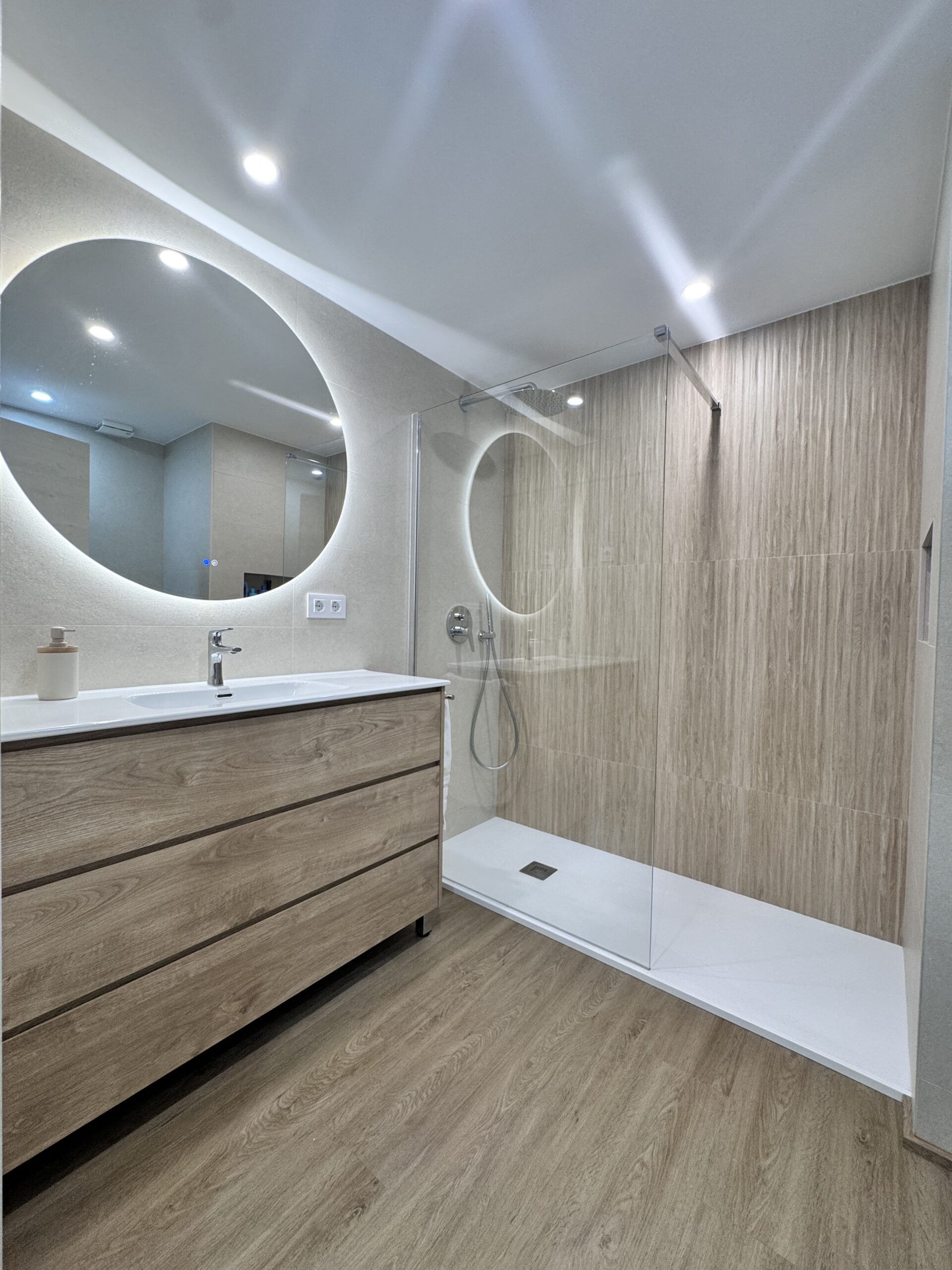 Reforma de baño en Esplugues realizada por Grup Innova. Ducha antideslizante, grifería empotrada, suelo vinílico SPC y diseño moderno en tonos madera y beige piedra.